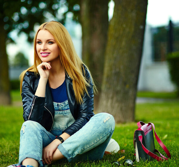 Портрет милой смешной блондинки современный сексуальный городской молодой стильной улыбающейся женщины модели в яркой современной ткани на открытом воздухе, сидя в парке в джинсах с розовым мешком
