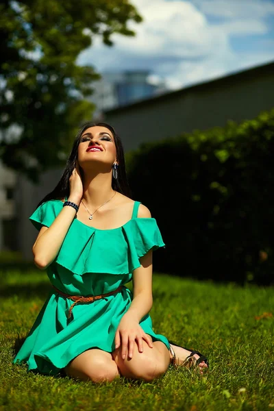 Портрет милой смешной сексуальной молодой стильной улыбающейся девушки модели в ярком современном зеленом платье с идеальным загорелым телом на открытом воздухе в парке — стоковое фото