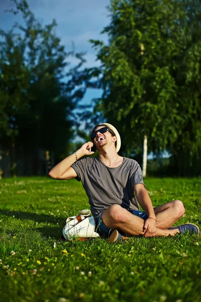 Casual kumaş şapkalı yeşil çimen parkta oturan gözlüklü genç çekici modern şık adam portresi — Stok fotoğraf