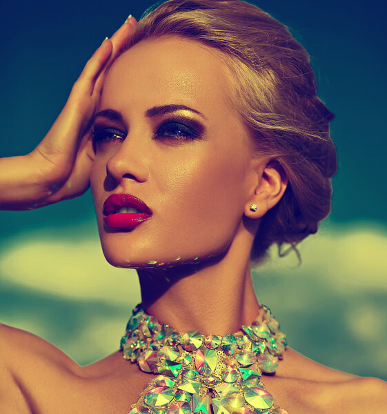 High fashion look.glamor sexy stylish blond young woman model with bright makeup and red lips with perfect sunbathed clean skin with jewelery outdoors in vogue style in evening dress behind blue sky