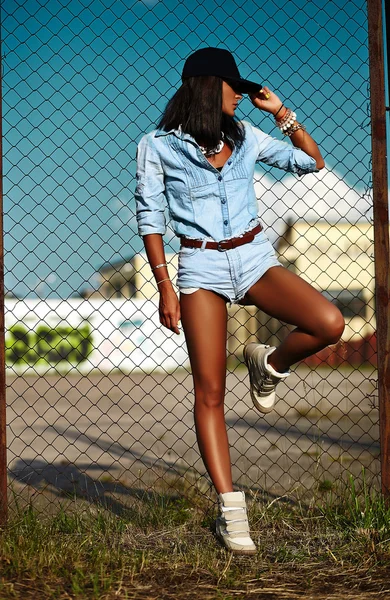 Portrait of sexy urban modern young stylish woman girl  model in casual jeans shorts  cloth outdoors in the street in black cap  behind blue sky — Stock Photo, Image