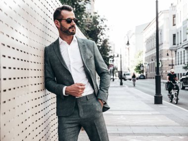 Yakışıklı, kendine güvenen, stil sahibi, Lambersex modelinin portresi. Zarif takım elbise giymiş modern bir adam. Moda erkeği gün batımında Avrupa şehrinin arka planında poz veriyor. Güneş gözlükleriyle
