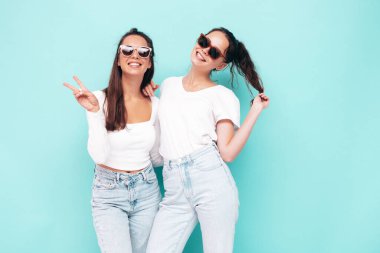 İki güzel, gülümseyen esmer hippi kadın moda yaz kıyafetleri içinde. Mavi duvarın yanında poz veren kaygısız seksi kadınlar. Pozitif modeller eğleniyor. Neşeli ve mutlu