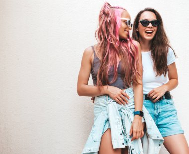 Son moda yaz kıyafetleri içinde iki güzel, gülümseyen hippi kadın. Pembe saçlı, sokakta poz veren kaygısız kadınlar. Pozitif saf modeller gün batımında eğleniyorlar. Neşeli ve mutlu