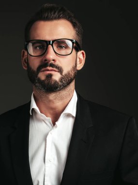 Yakışıklı, kendine güvenen, stil sahibi hipster Lambersex modelinin portresi. Zarif siyah takım elbiseli seksi modern adam. Moda erkeği karanlık arka planda stüdyoda poz veriyor. Gözlüklerle