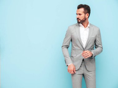Yakışıklı, kendine güvenen, stil sahibi, Lambersex modelinin portresi. Zarif takım elbise giymiş modern bir adam. Moda erkeği stüdyoda mavi duvarın yanında poz veriyor. 