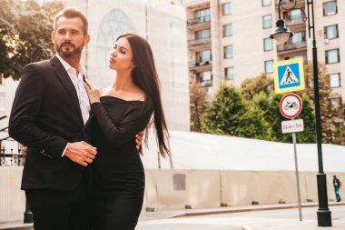 Güzel moda kadını ve takım elbiseli yakışıklı erkek arkadaşı. Siyah gece elbisesi içinde seksi esmer manken. Avrupa 'da sokakta poz veren şık bir çift. Vahşi adam ve dişisi açık havada