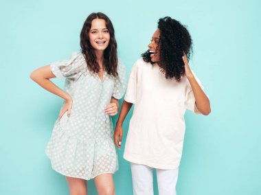 Moda kıyafetleri içinde iki güzel, gülümseyen uluslararası hippi kadın. Stüdyoda mavi duvarın yanında poz veren kaygısız seksi kadınlar. Pozitif modeller eğleniyor. Arkadaşlık kavramı