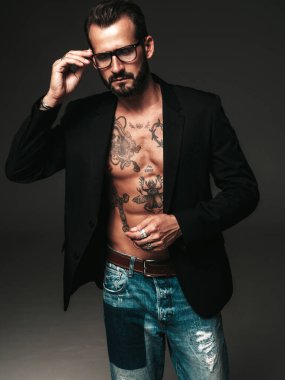 Yakışıklı, kendine güvenen, stil sahibi hipster Lambersex modelinin portresi. Siyah ceket giyen seksi modern adam. Dövmeli çıplak gövde. Stüdyoda siyah arka planda poz veren moda erkek. Gözlüklerle
