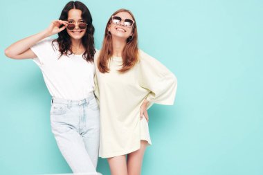 İki güzel, gülümseyen esmer hippi kadın moda yaz kıyafetleri içinde. Mavi duvarın yanında poz veren kaygısız seksi kadınlar. Pozitif modeller eğleniyor. Neşeli ve mutlu. Güneş gözlükleriyle