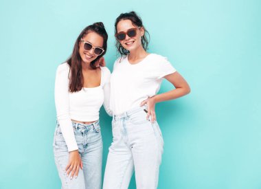 İki güzel, gülümseyen esmer hippi kadın moda yaz kıyafetleri içinde. Mavi duvarın yanında poz veren kaygısız seksi kadınlar. Pozitif modeller eğleniyor. Neşeli ve mutlu güneş gözlükleriyle