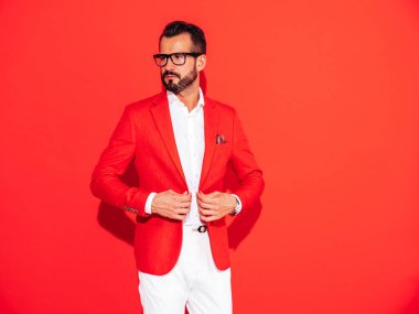 Yakışıklı, kendine güvenen, stil sahibi hipster Lambersex modelinin portresi. Zarif takım elbiseli seksi modern adam. Gözlüklü, kırmızı duvarın yanındaki stüdyoda poz veren modacı erkek.