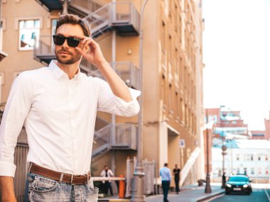 Yakışıklı, kendine güvenen, stil sahibi, Lambersex mankeni portresi. Beyaz gömlek giymiş modern bir adam. Sokakta poz veren düşünceli bir erkek. Gün batımında güneş gözlükleriyle dışarıda.