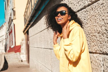 Saçları kıvırcık, güzel siyah kadın. Sarı kapüşonlu hippi modeli. Sokakta güneş gözlükleriyle poz veren kaygısız seksi kadın. Neşeli ve mutlu