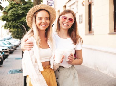 Son moda yaz kıyafetleri içinde iki güzel gülümseyen hippi kadın. Sokakta poz veren kaygısız kadınlar. Pozitif saf modeller gün batımında eğleniyorlar. Kahve ya da çay içiyorlar.