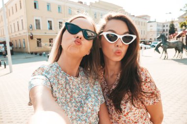 İki güzel, güler yüzlü yeniyetme kadın, modaya uygun yaz kıyafetleri içinde. Sokakta poz veren kaygısız kadınlar. Pozitif modeller canlı yayında öpüşüyor, Pov selfie çekiyor.