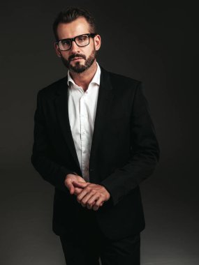Yakışıklı, kendine güvenen, stil sahibi hipster Lambersex modelinin portresi. Zarif siyah takım elbiseli seksi modern adam. Moda erkeği karanlık arka planda stüdyoda poz veriyor. Gözlüklerle