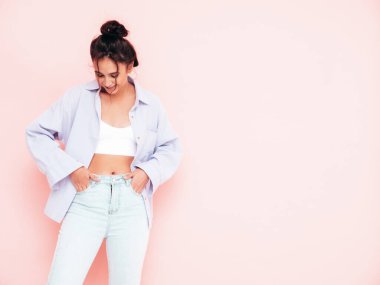 Moda kıyafetleri içinde gülümseyen güzel bir kadın. Stüdyoda pembe duvarın yanında poz veren kaygısız seksi kadın. Pozitif esmer model eğleniyor ve deliriyor. Neşeli ve mutlu 