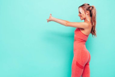 Pembe spor elbiseli, gülümseyen kadın portresi. Mükemmel vücutlu genç, güzel bir manken. Stüdyoda mavi duvarın yanında poz veren bir kadın. Neşeli ve mutlu. Eğitimden önce esniyorum.