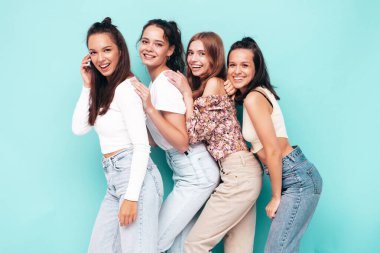 Dört güzel güzel, gülümseyen esmer hippi kadın moda yaz kıyafetleri içinde. Mavi duvarın yanında poz veren kaygısız seksi kadınlar. Pozitif modeller eğleniyor. Neşeli ve mutlu