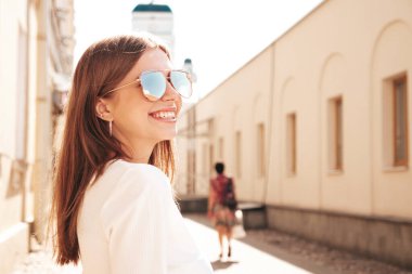 Moda kıyafetleri içinde gülümseyen genç ve güzel bir hippi kadın. Günbatımında sokakta poz veren kaygısız seksi kadın. Açık havada pozitif model. Neşeli ve mutlu güneş gözlükleriyle