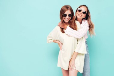 İki güzel, gülümseyen esmer hippi kadın moda yaz kıyafetleri içinde. Mavi duvarın yanında poz veren kaygısız seksi kadınlar. Pozitif modeller eğleniyor. Neşeli ve mutlu. Güneş gözlükleriyle