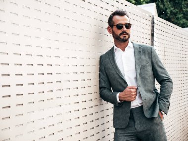 Yakışıklı, kendine güvenen, stil sahibi, lamberseksüel bir modelin portresi. Zarif takım elbise giymiş modern bir adam. Moda erkeği gün batımında Avrupa şehrinin arka planında poz veriyor. Güneş gözlükleriyle
