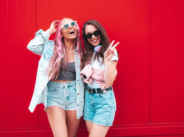 流行の夏服を着た2人の若い美しい笑顔のヒップスター女性 ピンクの髪を持つ赤い壁の近くの通りにポーズを取るセクシーな屈託のない女性 正の純粋なモデルは楽しんでいます 陽気で幸せ — ストック写真