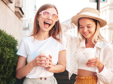 Son moda yaz kıyafetleri içinde iki güzel gülümseyen hippi kadın. Sokakta poz veren kaygısız kadınlar. Pozitif saf modeller gün batımında eğleniyorlar. Kahve ya da çay içiyorlar.