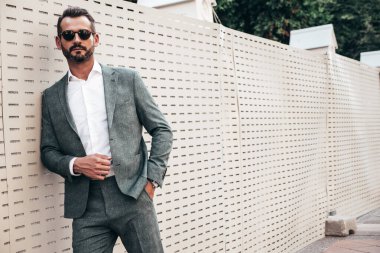Yakışıklı, kendine güvenen, stil sahibi, lamberseksüel bir modelin portresi. Zarif takım elbise giymiş modern bir adam. Moda erkeği gün batımında Avrupa şehrinin arka planında poz veriyor. Güneş gözlükleriyle