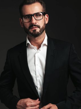 Yakışıklı, kendine güvenen, stil sahibi hipster Lambersex modelinin portresi. Zarif siyah takım elbiseli seksi modern adam. Moda erkeği karanlık arka planda stüdyoda poz veriyor. Gözlüklerle