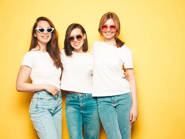 流行の夏の白いTシャツとジーンズの服で3人の若い美しい笑顔ヒップスター女性 スタジオで黄色の壁の近くにポーズ性的屈託のない女性 ポジティブモデル — ストック写真