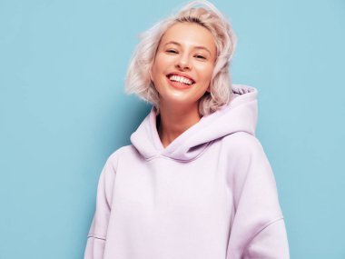 Son moda yaz kapüşonlu güzel, gülümseyen bir kadın. Stüdyoda mavi duvarın yanında poz veren kaygısız seksi kadın. Pozitif sarışın model eğleniyor ve deliriyor. Neşeli ve mutlu