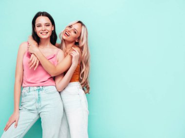 İki güzel, gülümseyen esmer hippi kadın moda yaz kıyafetleri içinde. Mavi duvarın yanında poz veren kaygısız seksi kadınlar. Pozitif modeller eğleniyor. Neşeli ve mutlu