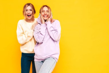 İki güzel, gülümseyen esmer hippi kadın moda yaz kıyafetleri içinde. Stüdyoda sarı duvarın yanında poz veren kaygısız seksi kadınlar. Pozitif modeller eğleniyor. Neşeli ve mutlu