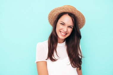 Moda kıyafetleri içinde gülümseyen güzel bir kadın. Stüdyoda mavi duvarın yanında poz veren kaygısız seksi kadın. Pozitif esmer model eğleniyor. Neşeli ve mutlu. Şapkalı.