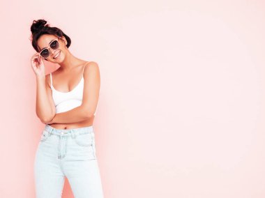 Moda kıyafetleri içinde gülümseyen güzel bir kadın. Stüdyoda pembe duvarın yanında poz veren kaygısız seksi kadın. Pozitif esmer model eğleniyor ve deliriyor. Neşeli ve mutlu 