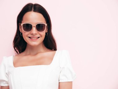 Moda kıyafetleri içinde gülümseyen güzel bir kadının yakın plan portresi. Stüdyoda pembe duvarın yanında poz veren kaygısız seksi kadın. Pozitif model içeride eğleniyor. Güneş gözlükleriyle