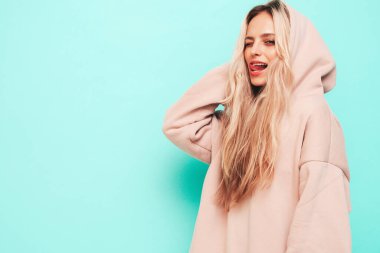 Son moda yaz kapüşonlu güzel, gülümseyen bir kadın. Stüdyoda mavi duvarın yanında poz veren kaygısız seksi kadın. Pozitif sarışın model eğleniyor ve deliriyor. Neşeli ve mutlu. Dilini gösterir