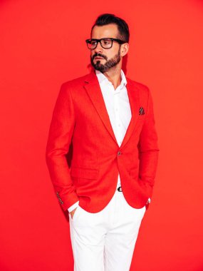 Yakışıklı, kendine güvenen, stil sahibi hipster Lambersex modelinin portresi. Zarif takım elbiseli seksi modern adam. Gözlüklü, kırmızı duvarın yanındaki stüdyoda poz veren modacı erkek.