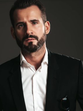 Yakışıklı, kendine güvenen, stil sahibi hipster Lambersex modelinin portresi. Zarif siyah takım elbiseli seksi modern adam. Moda erkeği karanlık arka planda stüdyoda poz veriyor. Kameraya bakıyorum. 
