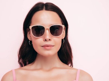 Moda kıyafetleri içinde kendine güvenen güzel bir kadının yakın plan portresi. Stüdyoda pembe duvarın yanında poz veren kaygısız seksi kadın. Pozitif model içeride eğleniyor. Güneş gözlükleriyle