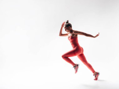 Pembe spor elbiseli kendine güvenen bir kadın. Mükemmel vücutlu genç ve güzel bir model. Stüdyoda beyaz bir kadın izole edilmiş. Neşeli ve mutlu. Zıpla ve koş.