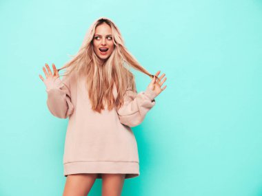 Son moda yaz kapüşonlu güzel, gülümseyen bir kadın. Stüdyoda mavi duvarın yanında poz veren kaygısız seksi kadın. Pozitif sarışın model eğleniyor ve deliriyor. Neşeli ve mutlu