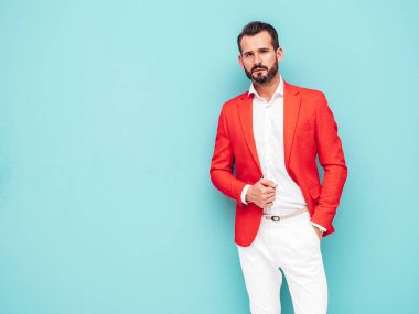Yakışıklı, kendine güvenen, stil sahibi, lamberseksüel modelin portresi. Zarif kırmızı takım elbise giymiş modern bir adam. Moda erkeği stüdyoda mavi duvarın yanında poz veriyor. 