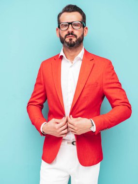 Yakışıklı, kendine güvenen, stil sahibi, lamberseksüel modelin portresi. Zarif kırmızı takım elbise giymiş modern bir adam. Moda erkeği mavi duvarın yanındaki stüdyoda poz veriyor.