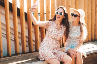 Son moda yaz kıyafetleri içinde iki güzel gülümseyen yeniyetme kadın. Sokakta şapkalı kayla poz veren kaygısız kadınlar. Pozitif saf modeller gün batımında eğleniyorlar, sarılıyorlar. Selfie çekiyoruz.