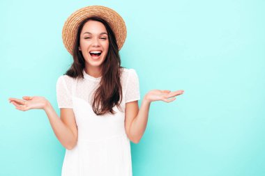 Genç, güzel, gülümseyen kadın. Stüdyoda şapka ve elbiseyle mavi duvarın yanında poz veren kaygısız seksi kadın. Pozitif model içeride eğleniyor. Ellerinizi kaldırın. Seçimi düşünüyorum. Şok oldum ve şaşırdım. 