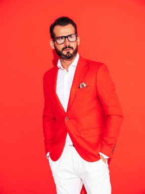 Yakışıklı, kendine güvenen, stil sahibi hipster Lambersex modelinin portresi. Zarif takım elbiseli seksi modern adam. Gözlüklü, kırmızı duvarın yanındaki stüdyoda poz veren modacı erkek.