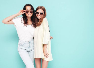 İki güzel, gülümseyen esmer hippi kadın moda yaz kıyafetleri içinde. Mavi duvarın yanında poz veren kaygısız seksi kadınlar. Pozitif modeller eğleniyor. Neşeli ve mutlu. Güneş gözlükleriyle